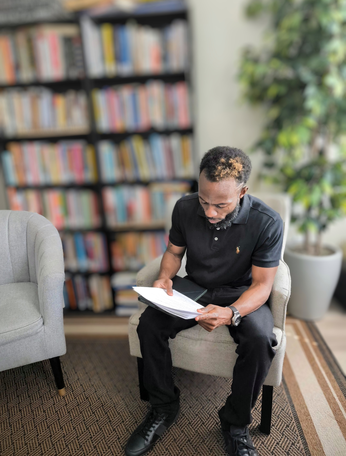 Jalal Wilson reading a book in his office with bookshelves behind him at StoryStack Studio